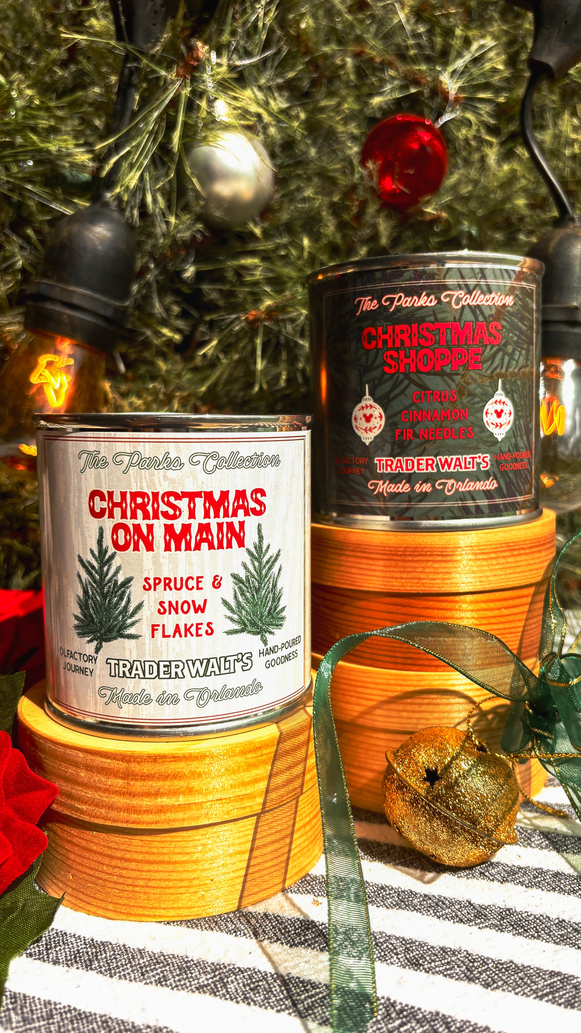 Disney-inspired Christmas on Main candle held in front of a decorated holiday tree. Trader Walt’s candle label features spruce branches and festive design, evoking Main Street Christmas and Mickey-style holiday magic.