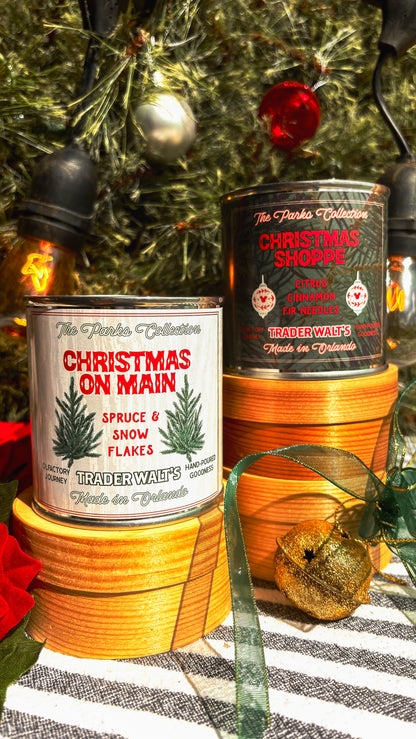 Disney-inspired Christmas on Main candle held in front of a decorated holiday tree. Trader Walt’s candle label features spruce branches and festive design, evoking Main Street Christmas and Mickey-style holiday magic.
