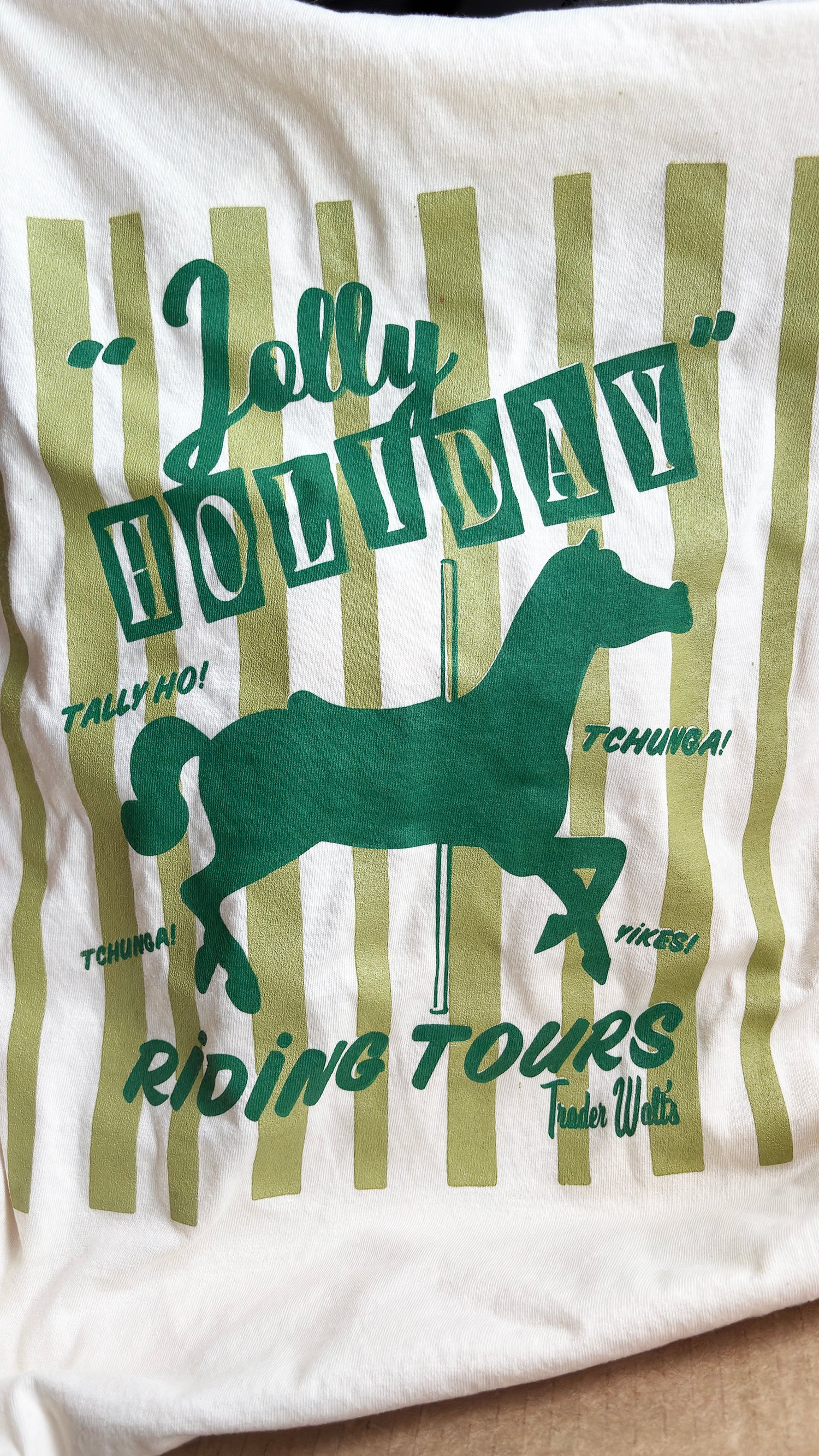 Vintage Jolly Holiday Riding Tours T-shirt with green carousel horse graphic and retro stripe background on cream cotton.