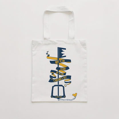 White tote bag with a screen printed navy and gold design of a keyblade wrapped in a flowing ribbon banner that reads May Your Heart Be Your Guiding Key