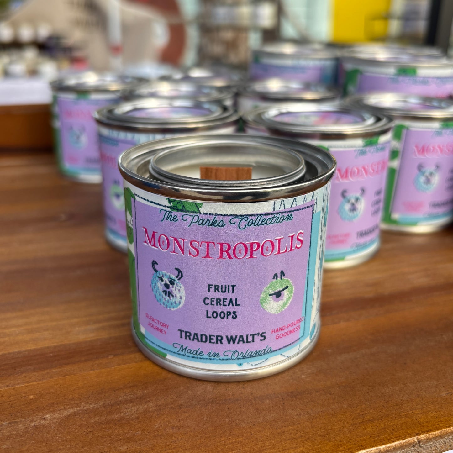 Close-up of the Monstropolis candle label showing pastel monster-themed artwork on a hand-poured citrus and cereal-scented tin candle.