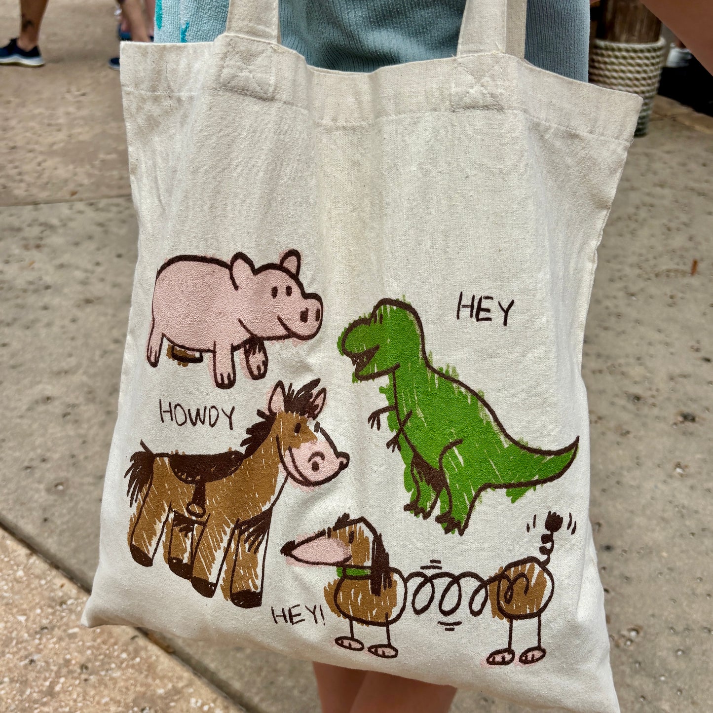 Toy Story inspired tote bag with crayon-style drawings of Rex, Hamm, Bullseye, and Slinky Dog on off-white cotton canvas